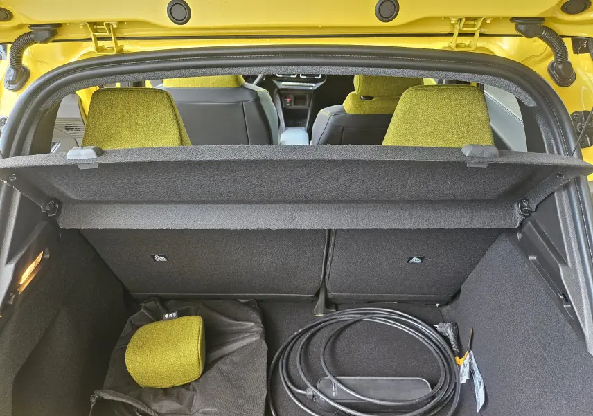 Coffre ouvert d'une Renault R5 électrique jaune pop, vue arrière montrant les sièges verts et un câble de recharge.