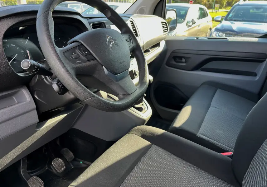 Vue intérieure côté conducteur du Citroën Jumpy 2022, volant noir, sièges gris et tableau de bord clair.