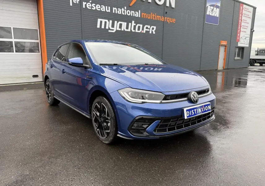 Volkswagen Polo 1.0 TSI R-Line bleu récif métallisé vue 3/4 avant droit sur sol mouillé devant un bâtiment.