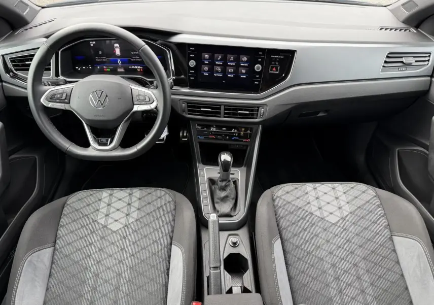 Intérieur avant de la Volkswagen Polo 2025, volant cuir multifonction, écran tactile 8 pouces et sièges tissu gris à motifs.