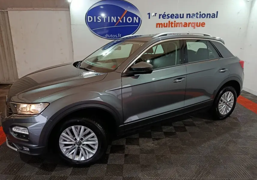 Volkswagen T-Roc gris foncé vue de profil droit en intérieur, avec jantes alliage et barres de toit chromées.