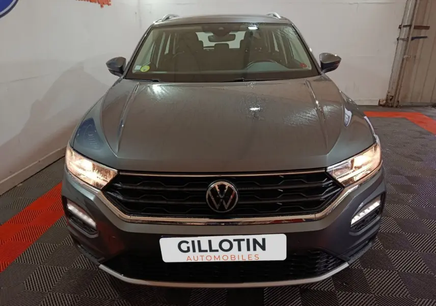 Vue frontale d’un Volkswagen T-Roc gris foncé avec feux allumés et calandre hexagonale distinctive.