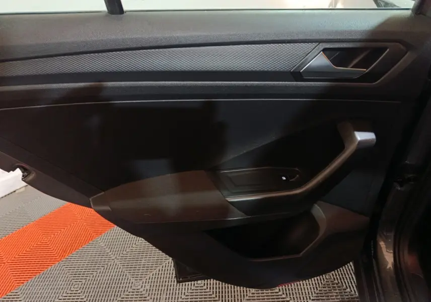 Vue intérieure côté gauche de la porte avant d’un Volkswagen T-Roc gris foncé, avec poignée et commande de lève-vitre.