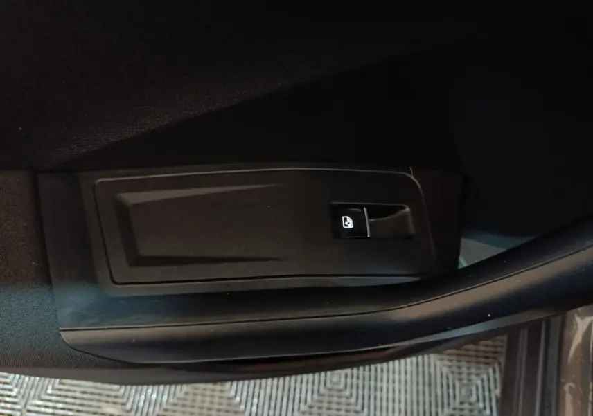 Gros plan sur le bouton d'ouverture de coffre noir, côté intérieur de porte d'un Volkswagen T-Roc gris foncé.