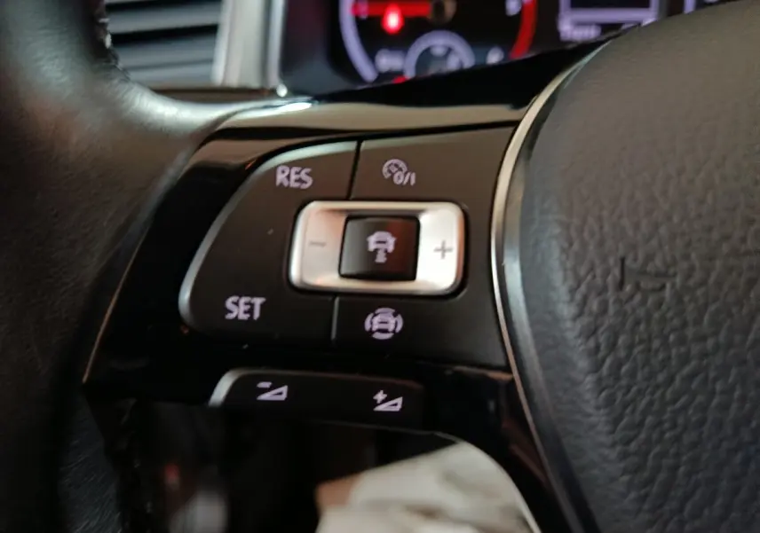 Gros plan sur les commandes de régulateur de vitesse au volant cuir noir du Volkswagen T-Roc 2.0 TDI 150 gris foncé.