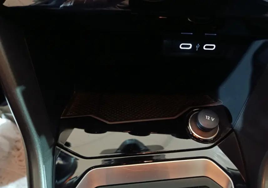 Gros plan sur la console centrale noire brillante du Volkswagen T-Roc 2.0 TDI avec prise 12V et ports USB éclairés.