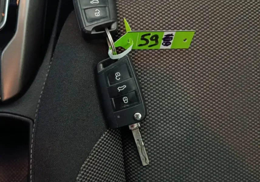 Gros plan sur deux clés Volkswagen posées sur un siège tissu gris à motifs, avec une étiquette verte attachée.