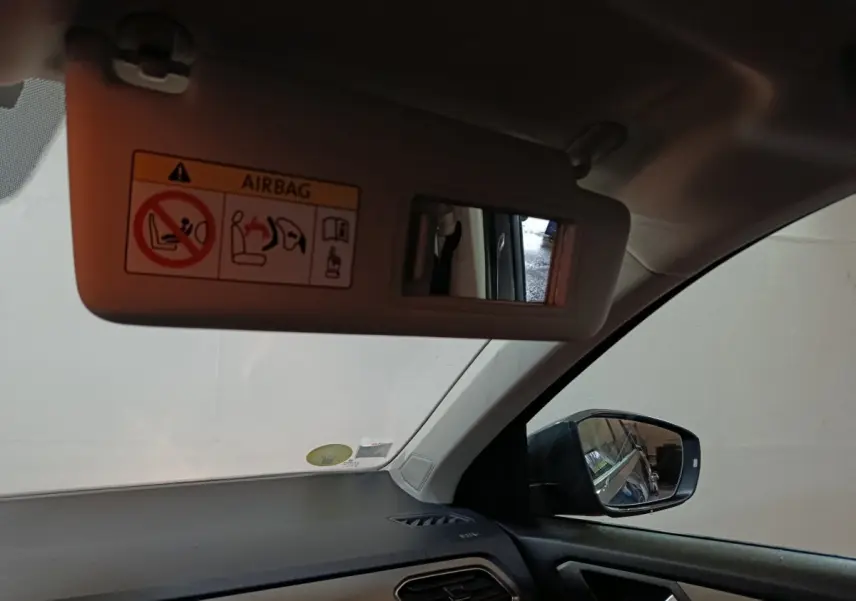 Vue intérieure côté conducteur du Volkswagen T-Roc gris foncé, montrant le pare-soleil avec miroir et rétroviseur latéral droit.