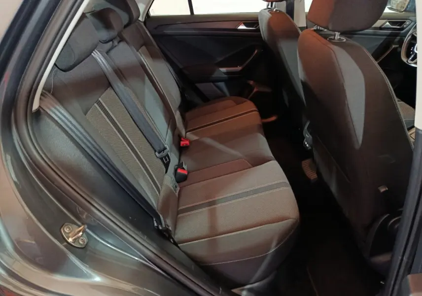 Vue intérieure côté arrière gauche du Volkswagen T-Roc gris foncé, montrant la banquette arrière en tissu avec ceintures de sécurité.