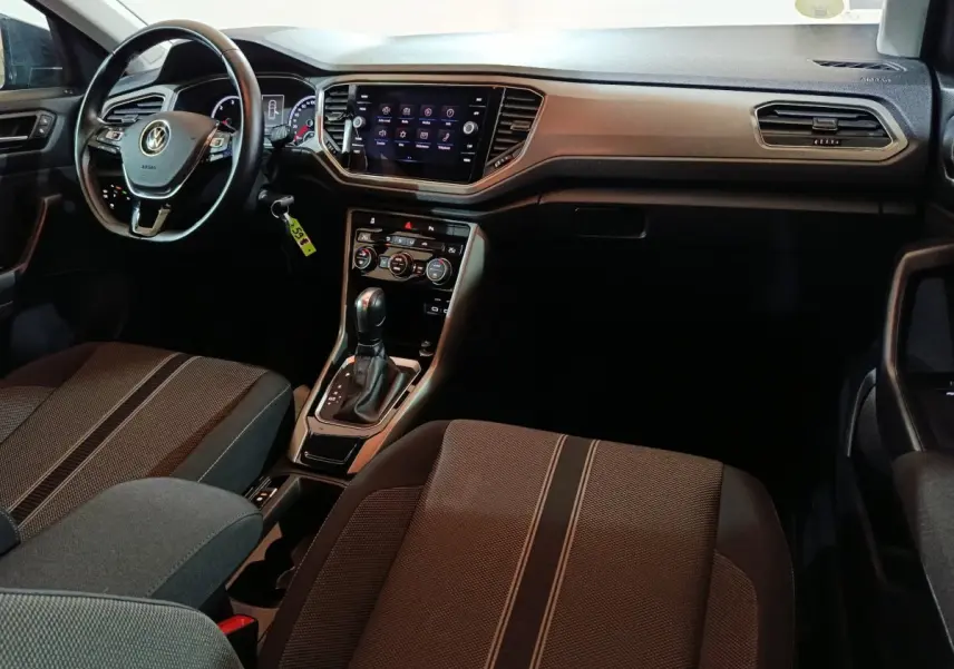 Vue intérieure côté conducteur du tableau de bord et console centrale du Volkswagen T-Roc gris foncé avec écran tactile et volant cuir.