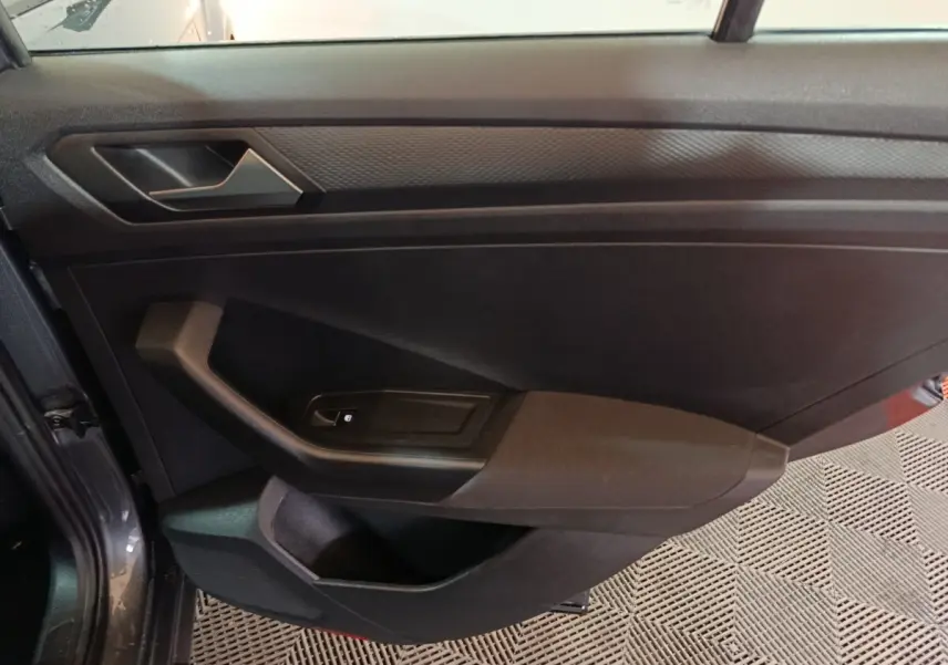 Vue intérieure de la porte côté gauche du Volkswagen T-Roc gris foncé, avec poignée et commande de lève-vitre.