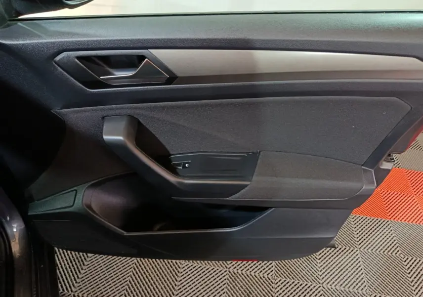Vue rapprochée de la porte côté gauche du Volkswagen T-Roc gris foncé, montrant la poignée intérieure et les commandes.