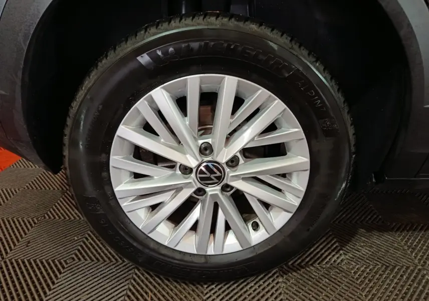 Gros plan sur la roue avant droite d’un Volkswagen T-Roc gris foncé, jante alliage argentée à multiples branches.