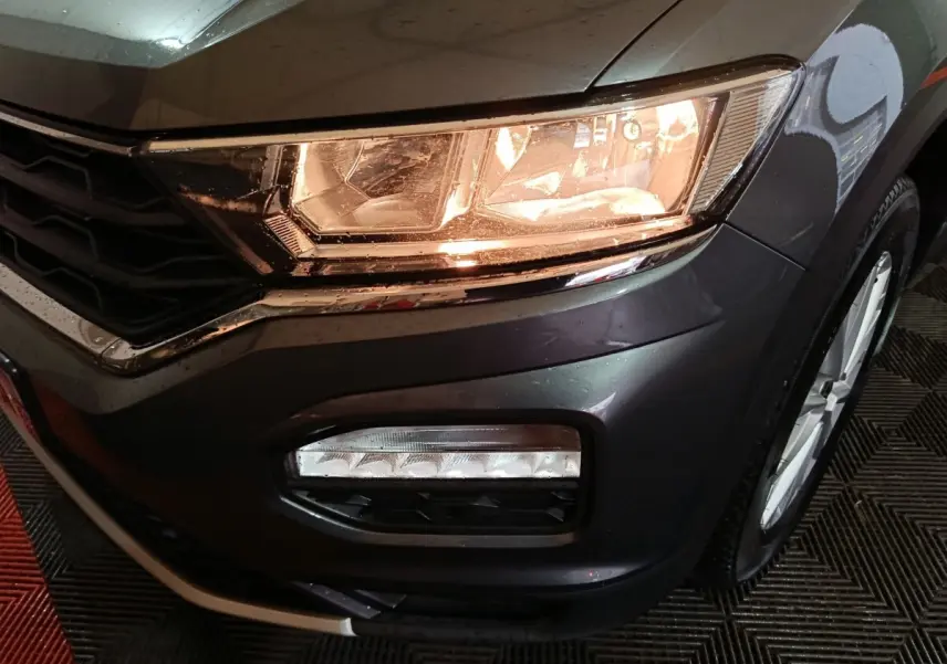 Gros plan sur l'avant droit gris foncé du Volkswagen T-Roc 2021, mettant en valeur le phare allumé et le feu antibrouillard.
