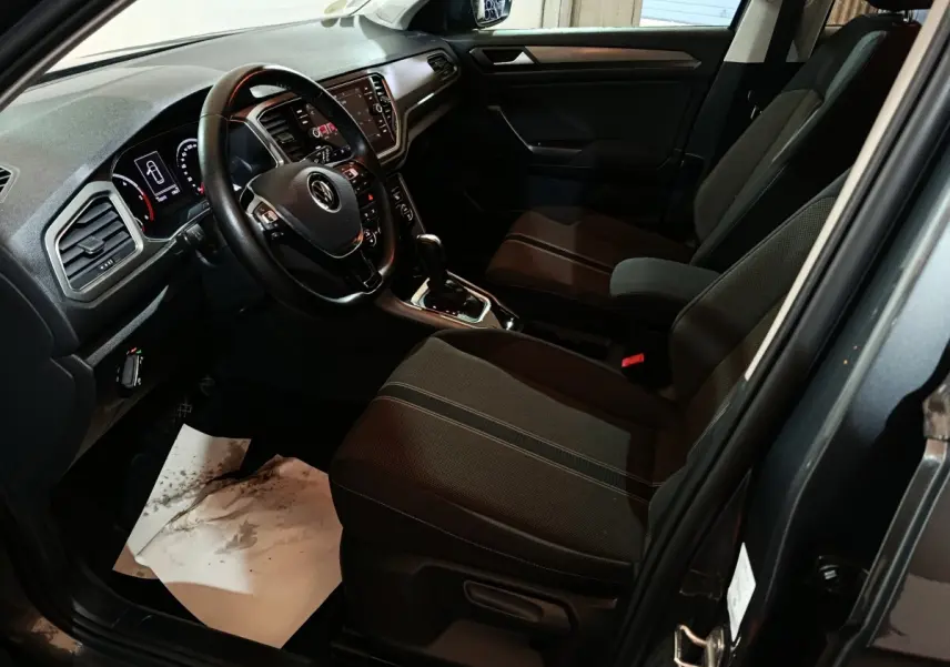 Vue intérieure côté conducteur du Volkswagen T-Roc gris foncé, avec tableau de bord digital et volant cuir multifonctions.