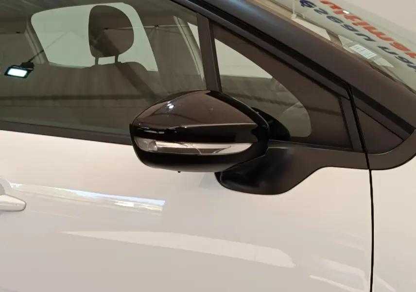 Gros plan sur le rétroviseur noir côté conducteur d'une Citroën C3 blanche, avec vitre teintée en arrière-plan.