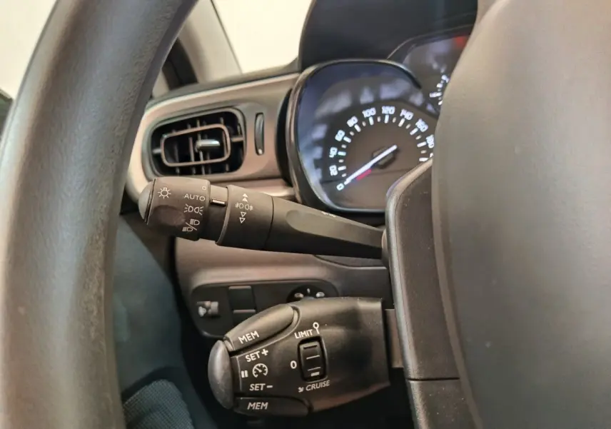 Vue rapprochée du tableau de bord côté gauche de la Citroën C3 blanche, montrant les commandes de régulateur et phares.