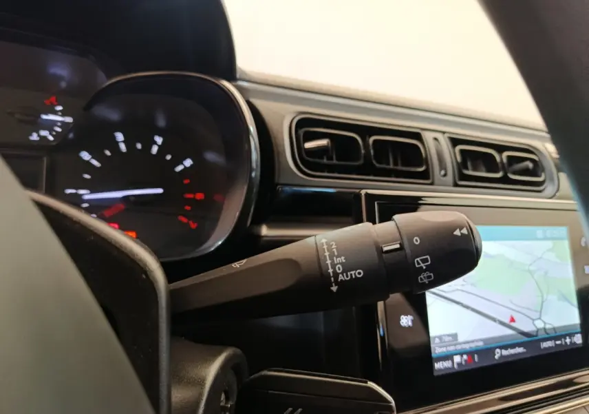 Détail du commodo d’essuie-glace dans l’habitacle d’une Citroën C3 blanche, avec tableau de bord et écran tactile de navigation.