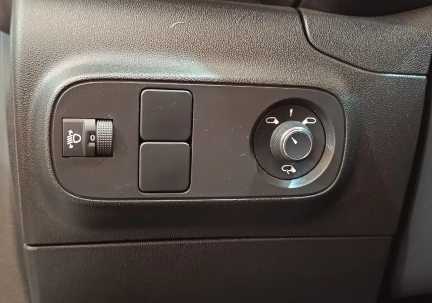 Gros plan sur les commandes de réglage des rétroviseurs et des phares dans l'habitacle noir d'une Citroën C3 blanche.
