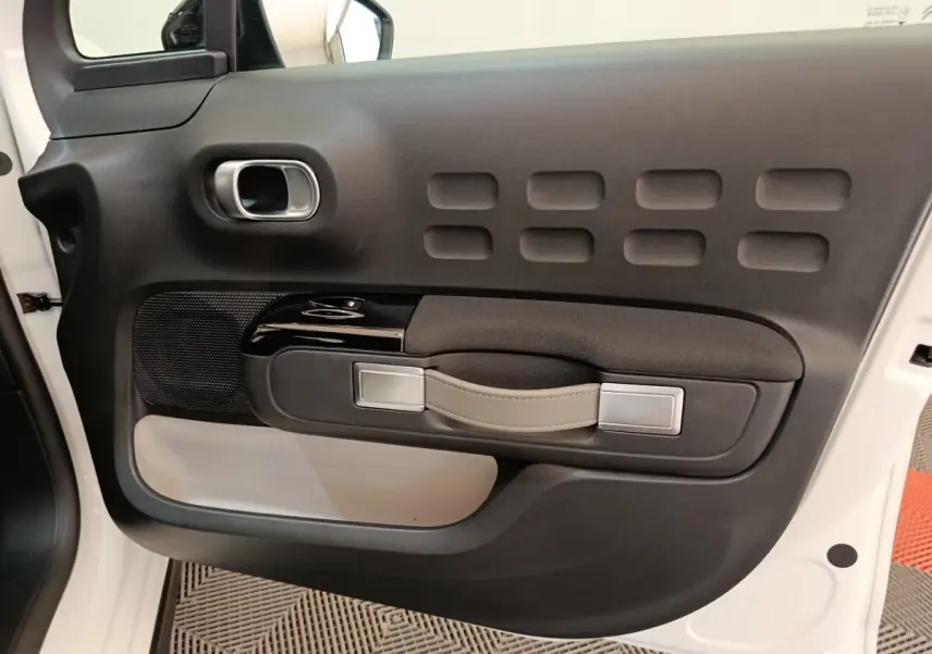 Vue intérieure côté gauche de la porte avant blanche de la Citroën C3 2020 avec poignée cuir et inserts noirs.