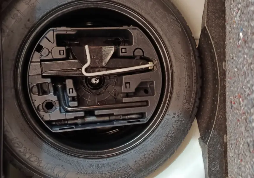 Vue rapprochée de la roue de secours noire et de ses outils, logée dans le coffre blanc d'une Citroën C3 2020.