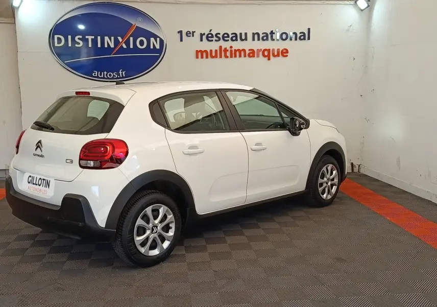 Vue 3/4 arrière droite d'une Citroën C3 blanche 2020 dans un showroom avec logo Distinxion en arrière-plan.