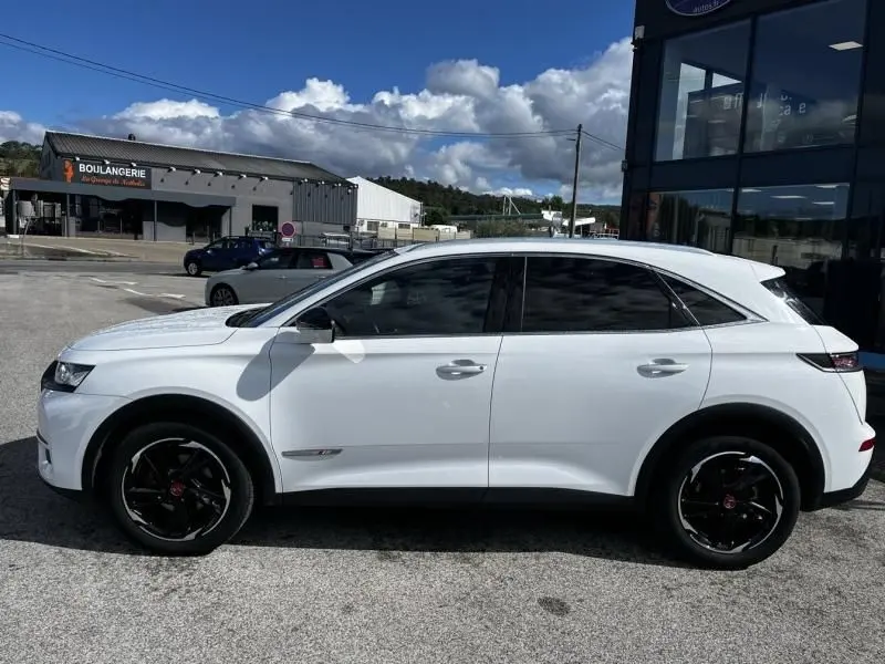 Vue de profil côté gauche d’un DS7 Crossback blanc 2019 avec jantes noires et vitres teintées, stationné en extérieur.