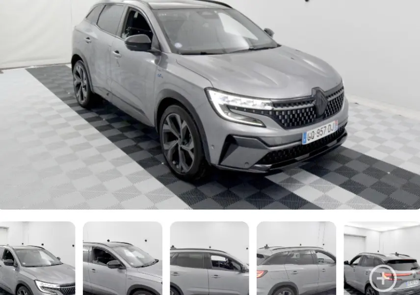 Vue 3/4 avant du Renault Austral gris avec jantes aluminium et barres de toit visibles en intérieur studio.