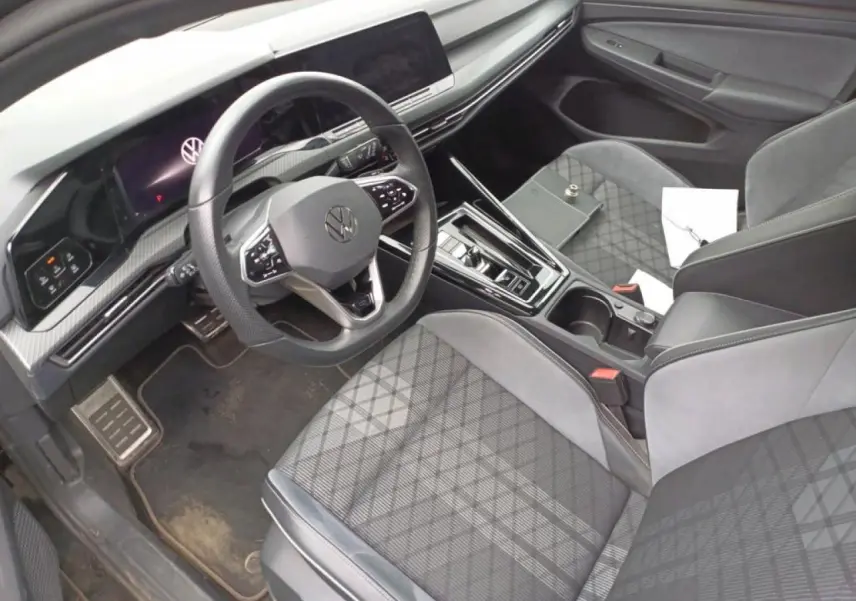 Vue intérieure côté conducteur de la Volkswagen Golf 8 R-Line 2024, sièges tissu noir et tableau de bord digital.