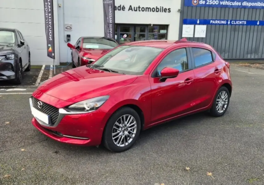 Vue 3/4 avant d'une Mazda2 rouge brillante avec jantes aluminium, stationnée devant un concessionnaire.