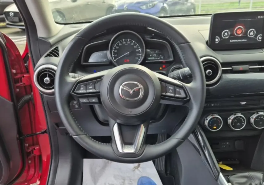 Vue intérieure centrée sur le volant cuir multifonctions de la Mazda2 rouge, avec tableau de bord et écran multifonction visibles.