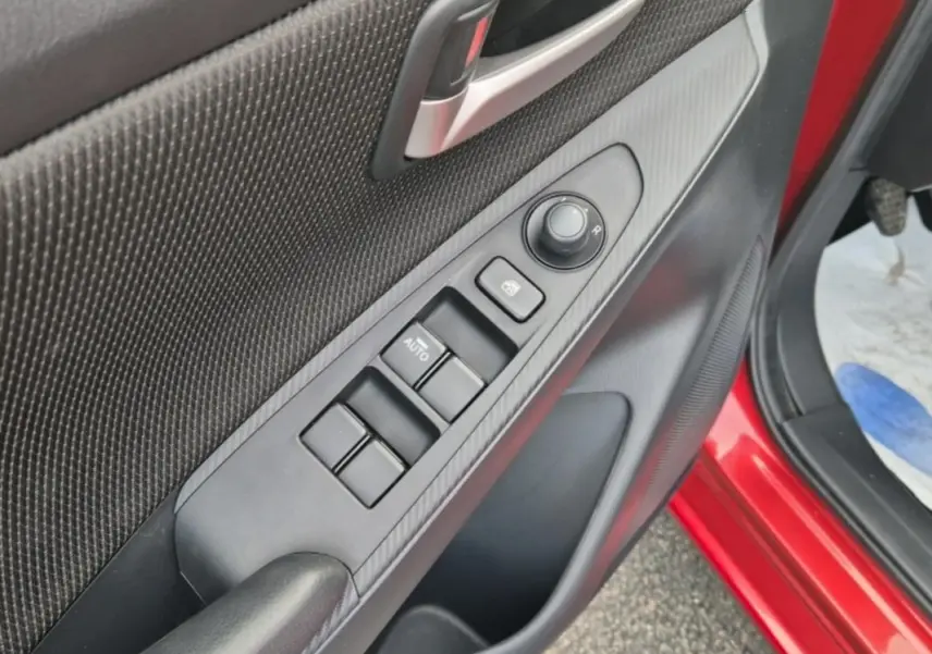 Gros plan sur la commande des vitres électriques côté conducteur d'une Mazda2 rouge avec finition intérieure noire.