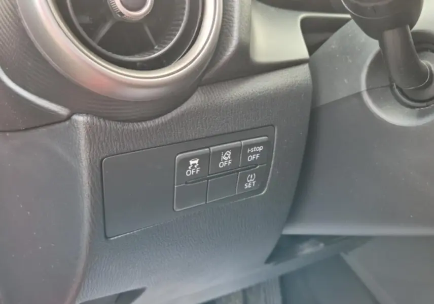 Gros plan sur les commandes de sécurité et l'aération côté gauche du tableau de bord noir d'une Mazda2 rouge 2021.