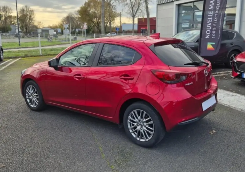 Vue 3/4 arrière droite d'une Mazda2 rouge 2021 avec jantes aluminium et vitres surteintées stationnée en extérieur.