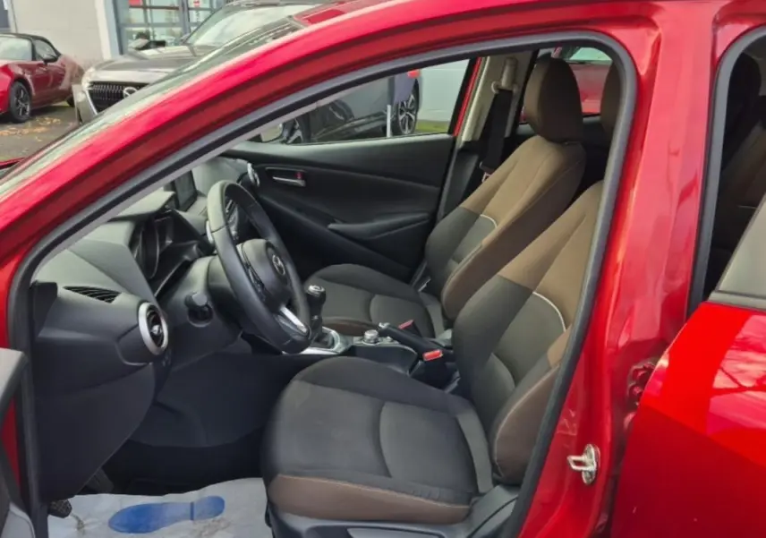 Vue intérieure côté conducteur de la Mazda2 rouge 2021, sièges bi-ton marron et noir avec volant multifonctions cuir.