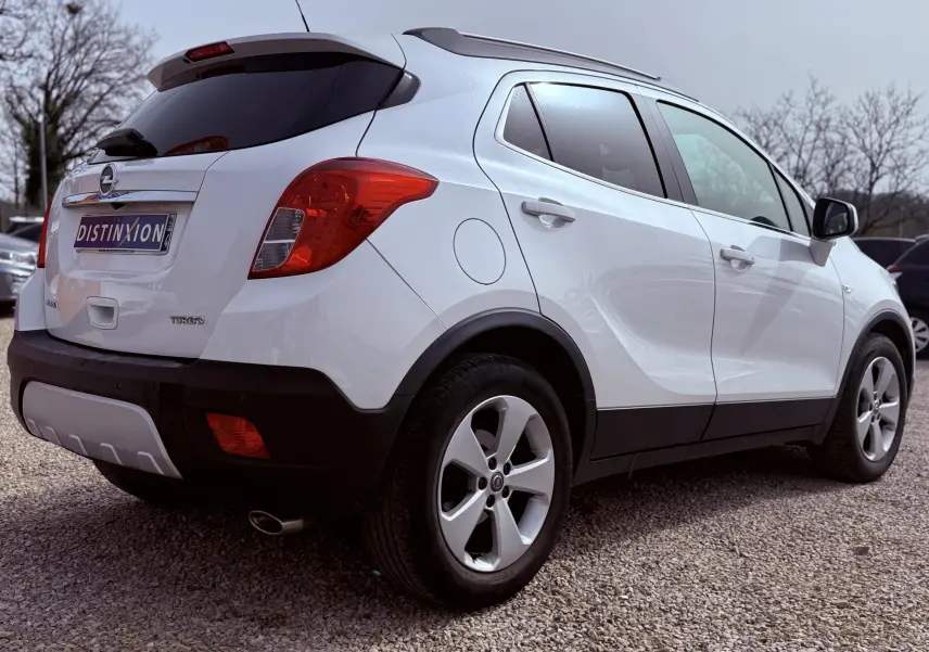 Vue 3/4 arrière droite d'un Opel Mokka X blanc avec jantes alliage et vitres teintées sur parking.