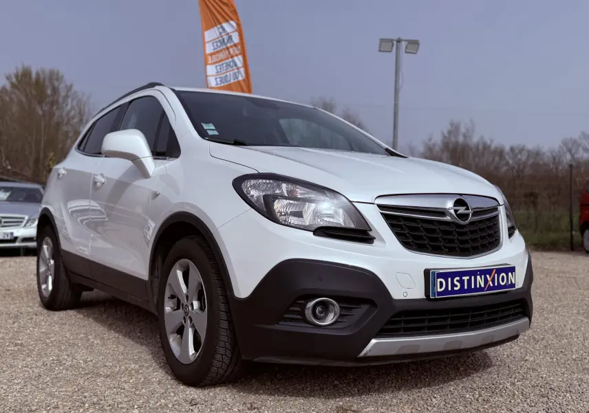 Opel Mokka X blanc vue 3/4 avant droit avec calandre noire et jantes argentées sur parking extérieur.
