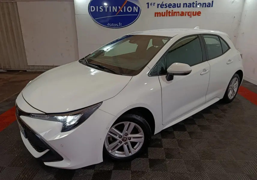 Toyota Corolla hybride blanche vue en 3/4 avant droit, avec phares LED et jantes alliage visibles.