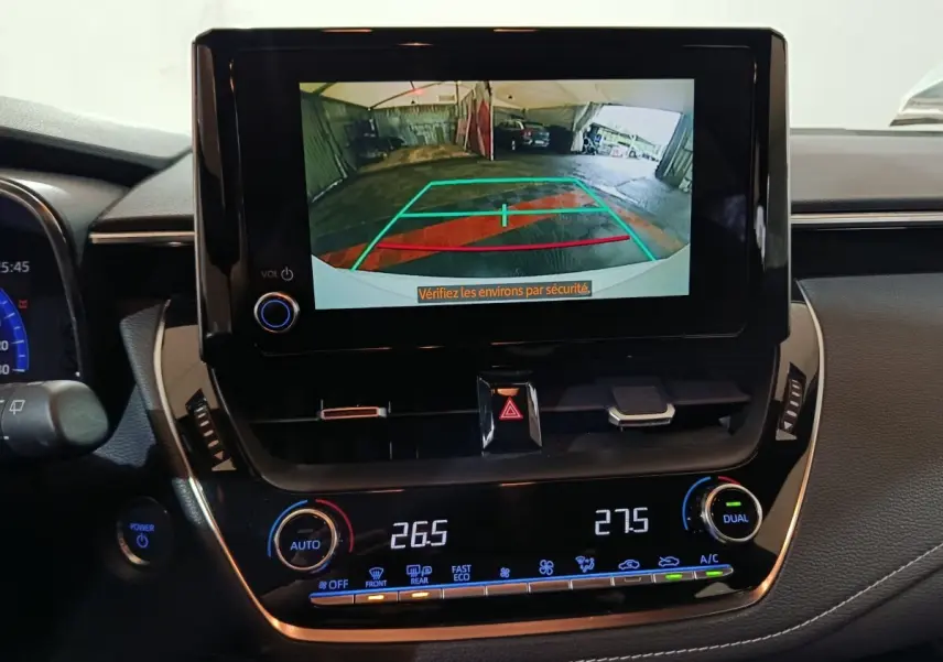 Vue intérieure du tableau de bord de la Toyota Corolla hybride blanche, avec écran de caméra de recul et commandes climatisation.
