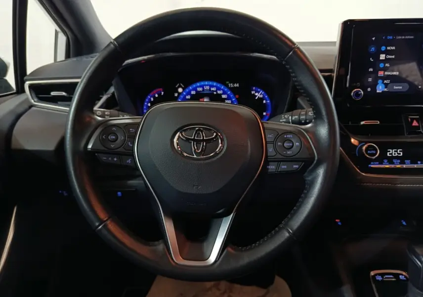 Vue intérieure centrée sur le volant cuir noir de la Toyota Corolla hybride 2022 avec tableau de bord et écran tactile visibles.