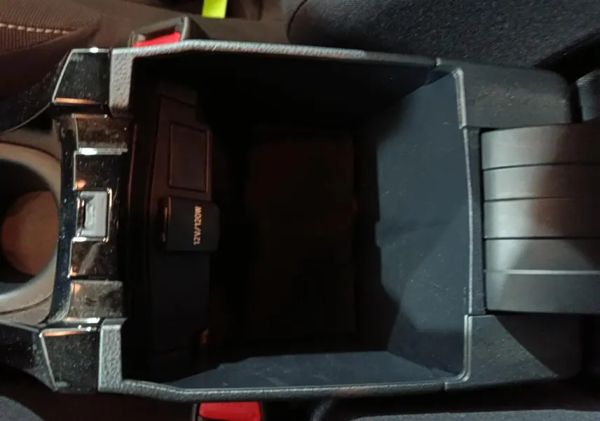 Vue plongeante sur le rangement central noir de la Toyota Corolla hybride 2022, avec prise 12V visible à l'intérieur.