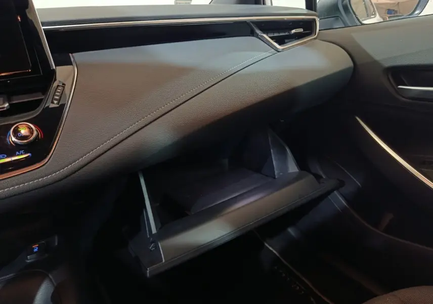 Intérieur de la Toyota Corolla Hybride 2022, vue côté passager sur la boîte à gants ouverte et tableau de bord noir.