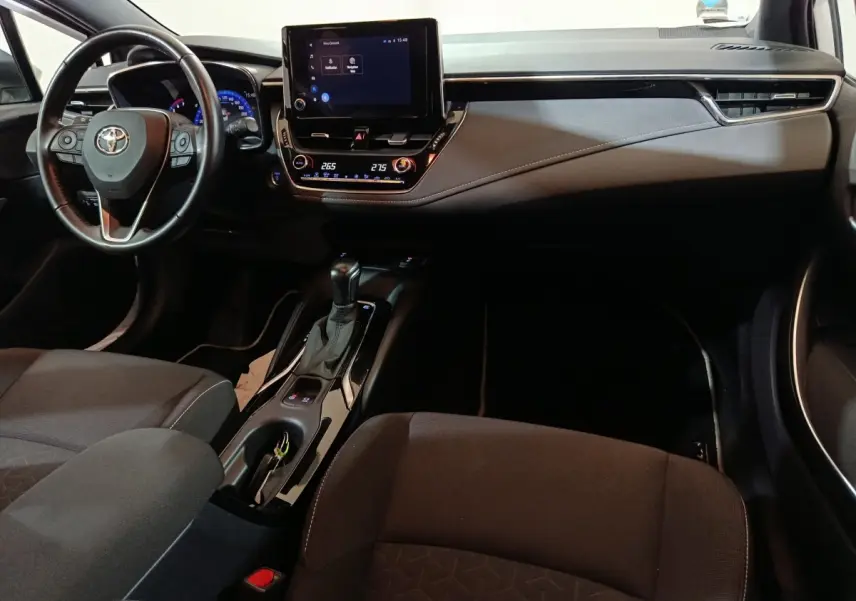 Vue intérieure avant de la Toyota Corolla hybride 2022, tableau de bord noir avec écran tactile central et volant cuir multifonctions.