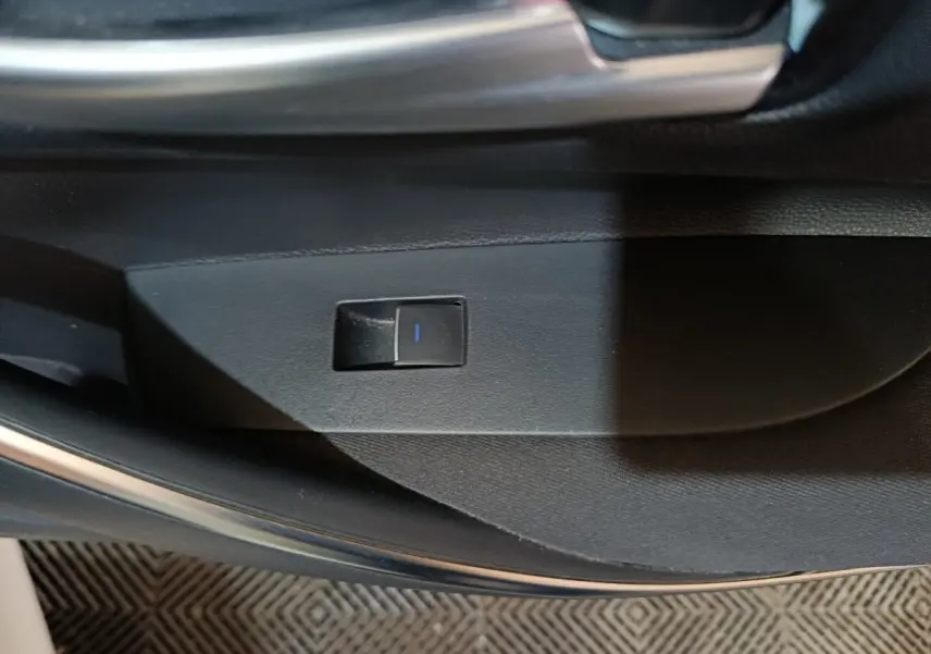 Gros plan sur le bouton de commande électrique de la portière intérieure d'une Toyota Corolla blanche, version hybride 2022.