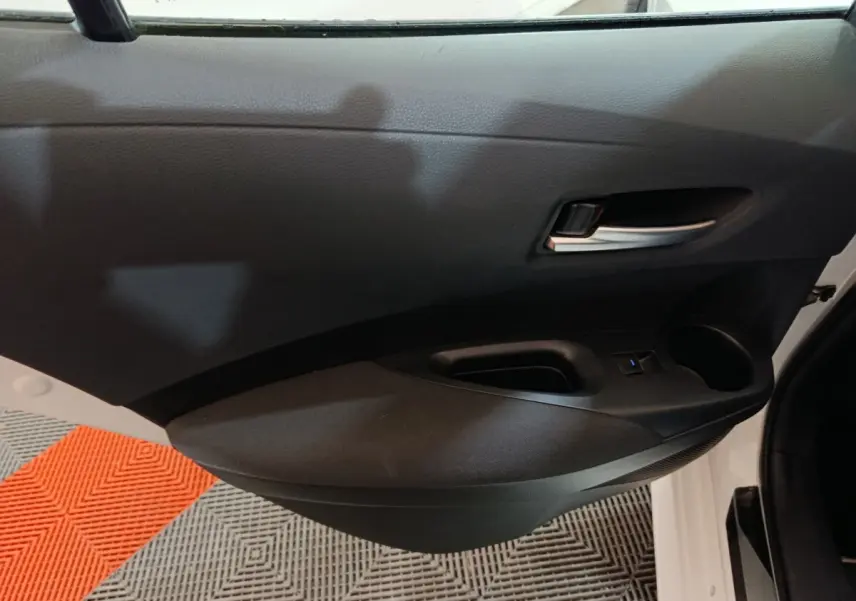 Vue intérieure côté gauche de la porte avant noire d'une Toyota Corolla hybride blanche, avec poignée et commande fenêtre.