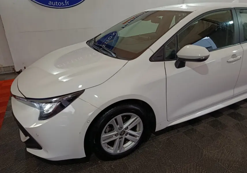 Vue 3/4 avant droit d'une Toyota Corolla hybride blanche avec phares LED et rétroviseurs électriques rabattables.