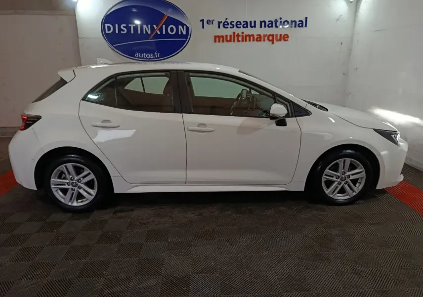 Profil latéral droit d'une Toyota Corolla hybride blanche 2022, avec jantes alliage et rétroviseurs électriques rabattables.