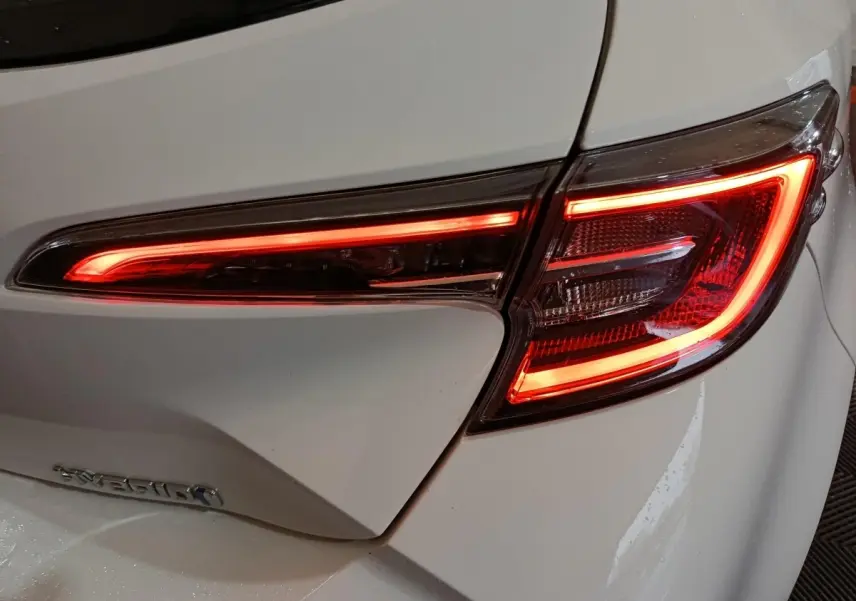 Gros plan sur le feu arrière droit allumé d'une Toyota Corolla hybride blanche, soulignant ses lignes LED distinctives.