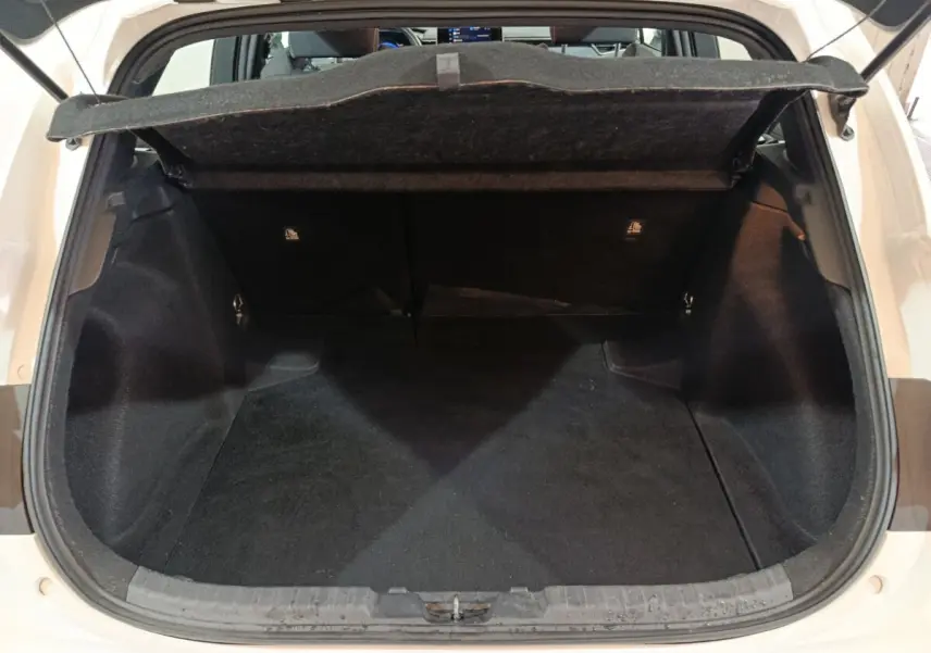 Vue arrière du coffre ouvert d'une Toyota Corolla hybride blanche, montrant l'espace de chargement vide et la tablette cache-bagages.