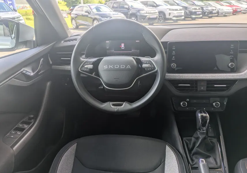 Vue intérieure centrée sur le volant SKODA avec tableau de bord numérique et écran tactile, ambiance moderne et épurée.